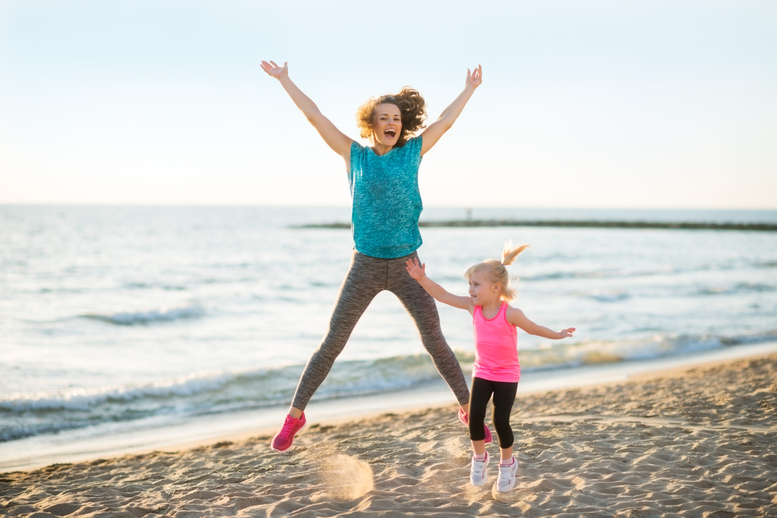 Madre e hija saltando en la playa